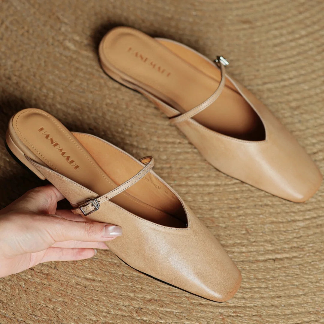 Pair of beige shoes with a hand holding one shoe on a textured surface