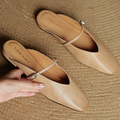 Pair of beige shoes with a hand holding one shoe on a textured surface