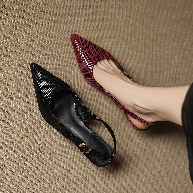 Black and burgundy pointed-toe shoes on a textured beige surface