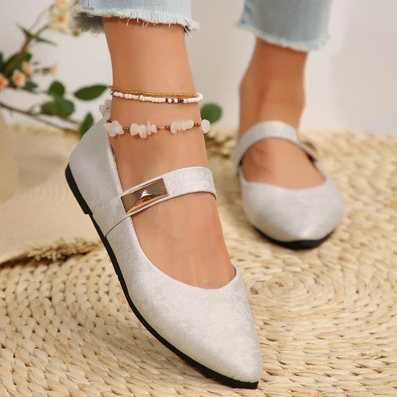 White pointed-toe shoes with a gold buckle on a woven surface