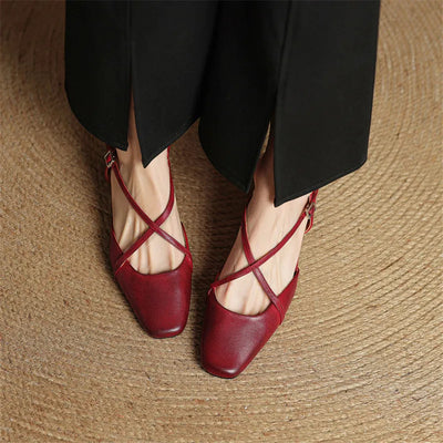 Red strappy shoes worn with black pants on a textured surface