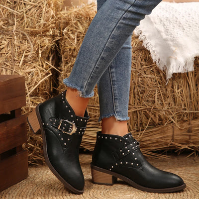 Black studded ankle boots worn with blue jeans against a rustic background