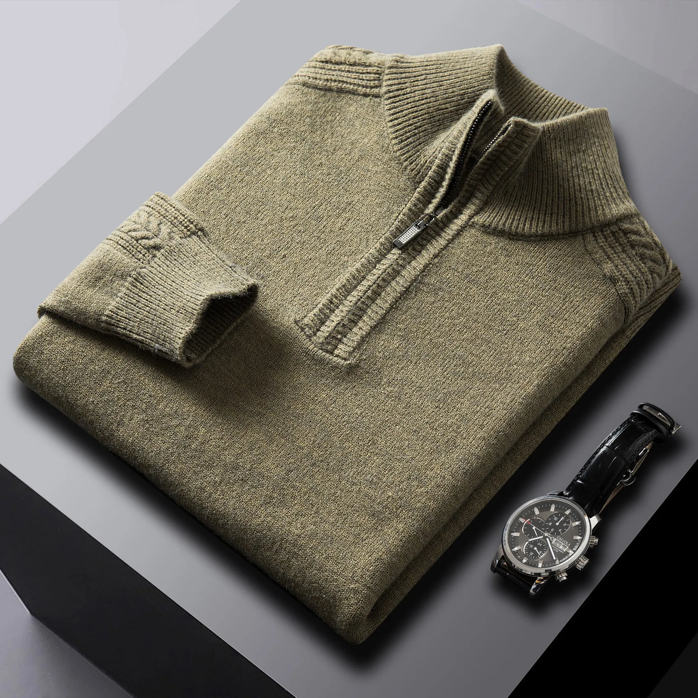 Folded olive green sweater with a watch on a gray surface