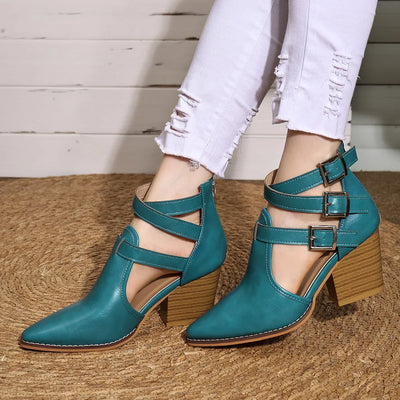Teal high-heeled shoes with wooden soles worn by a person on a wooden floor.