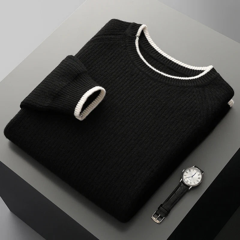 Folded black sweater with white trim on a gray surface next to a black watch.
