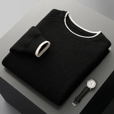 Folded black sweater with white trim on a gray surface next to a black watch.