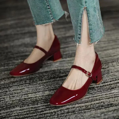 Red high-heeled shoes worn with light blue jeans on a textured floor.