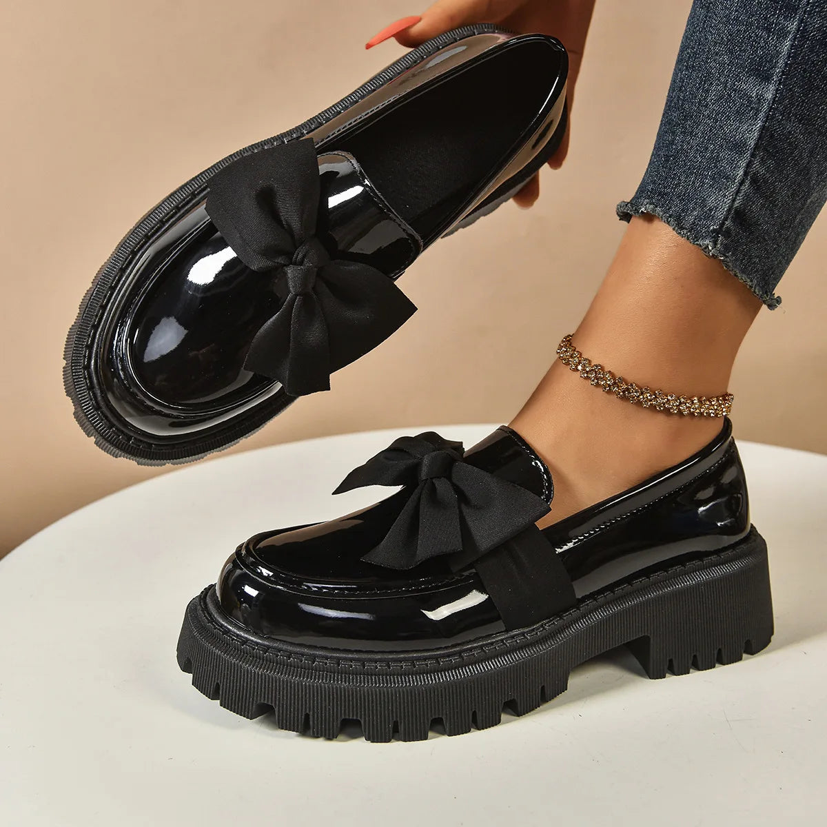 Black patent leather shoes with bows worn by a person on a beige background