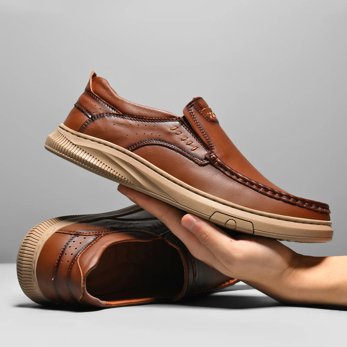 Brown leather shoes being held against a gray background
