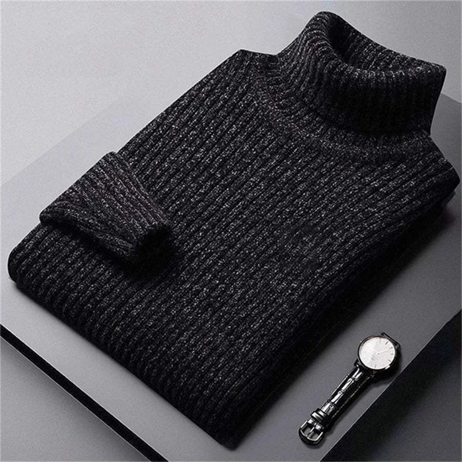 Folded black sweater on a gray surface with a silver button beside it