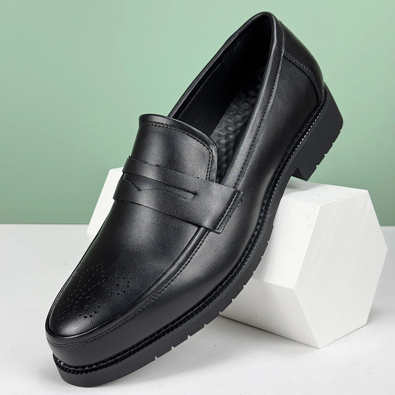 Black leather loafer shoe on a white block with a light green background