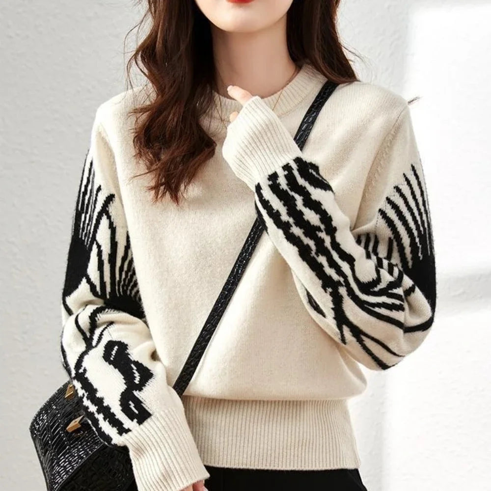 Person wearing a cream sweater with black patterned sleeves against a plain background