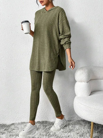 Person wearing a green ribbed sweater and pants set, holding a coffee cup against a white background.