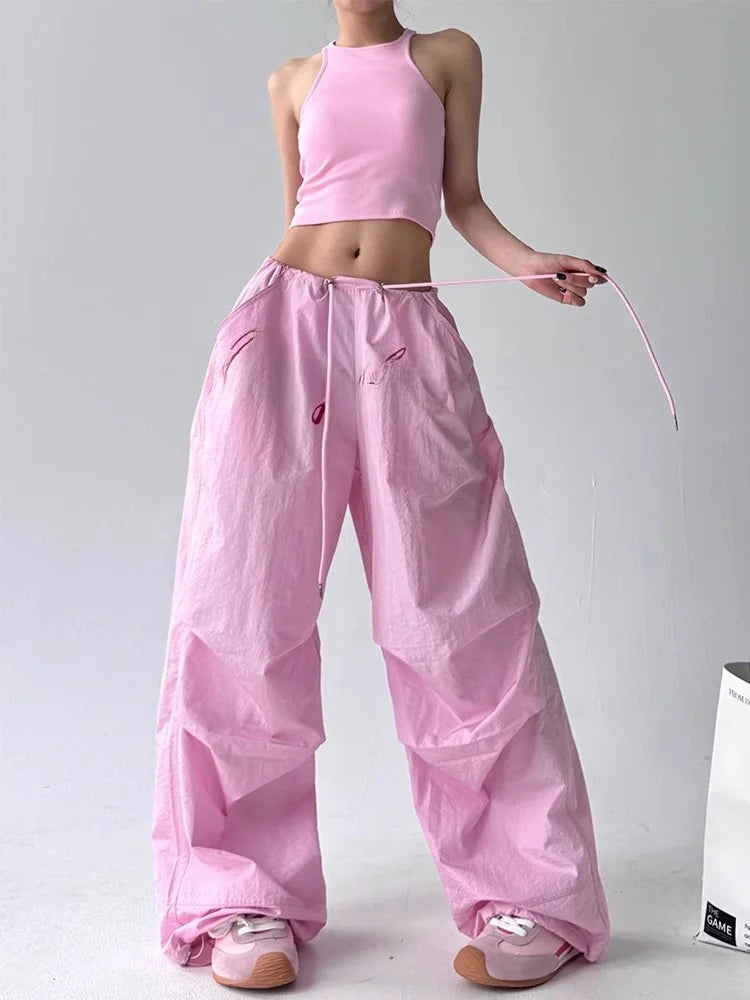 Person wearing a pink outfit with wide-leg pants and a crop top on a plain background