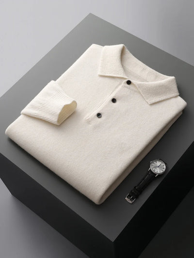 Folded cream-colored polo shirt with black buttons on a gray surface, accompanied by a watch.