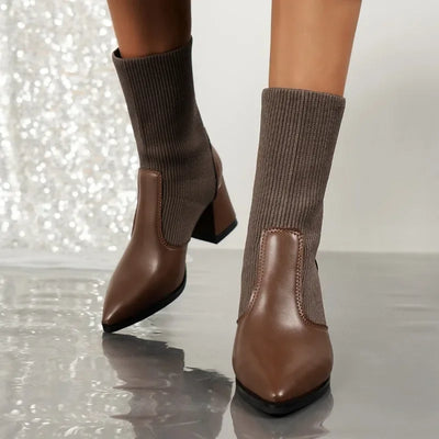 Brown ankle boots with sock-like tops worn by a person on a reflective surface.