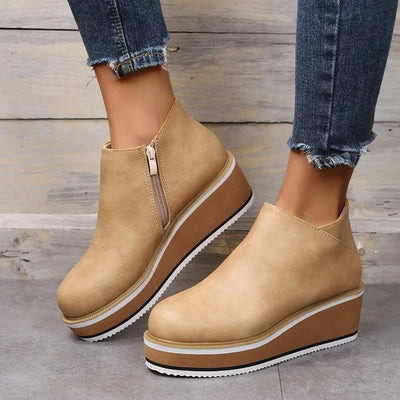 Beige wedge ankle boots worn with blue jeans on a wooden floor.