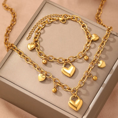 Gold chain necklace with heart-shaped pendants on a beige surface