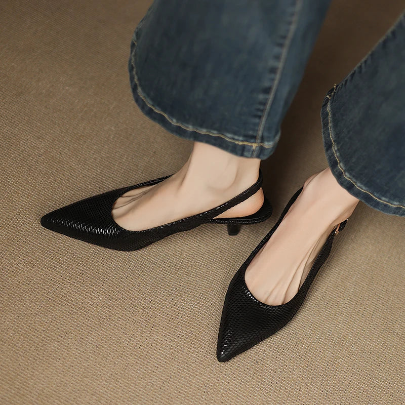 Black pointed-toe shoes worn with blue jeans on a beige carpet.