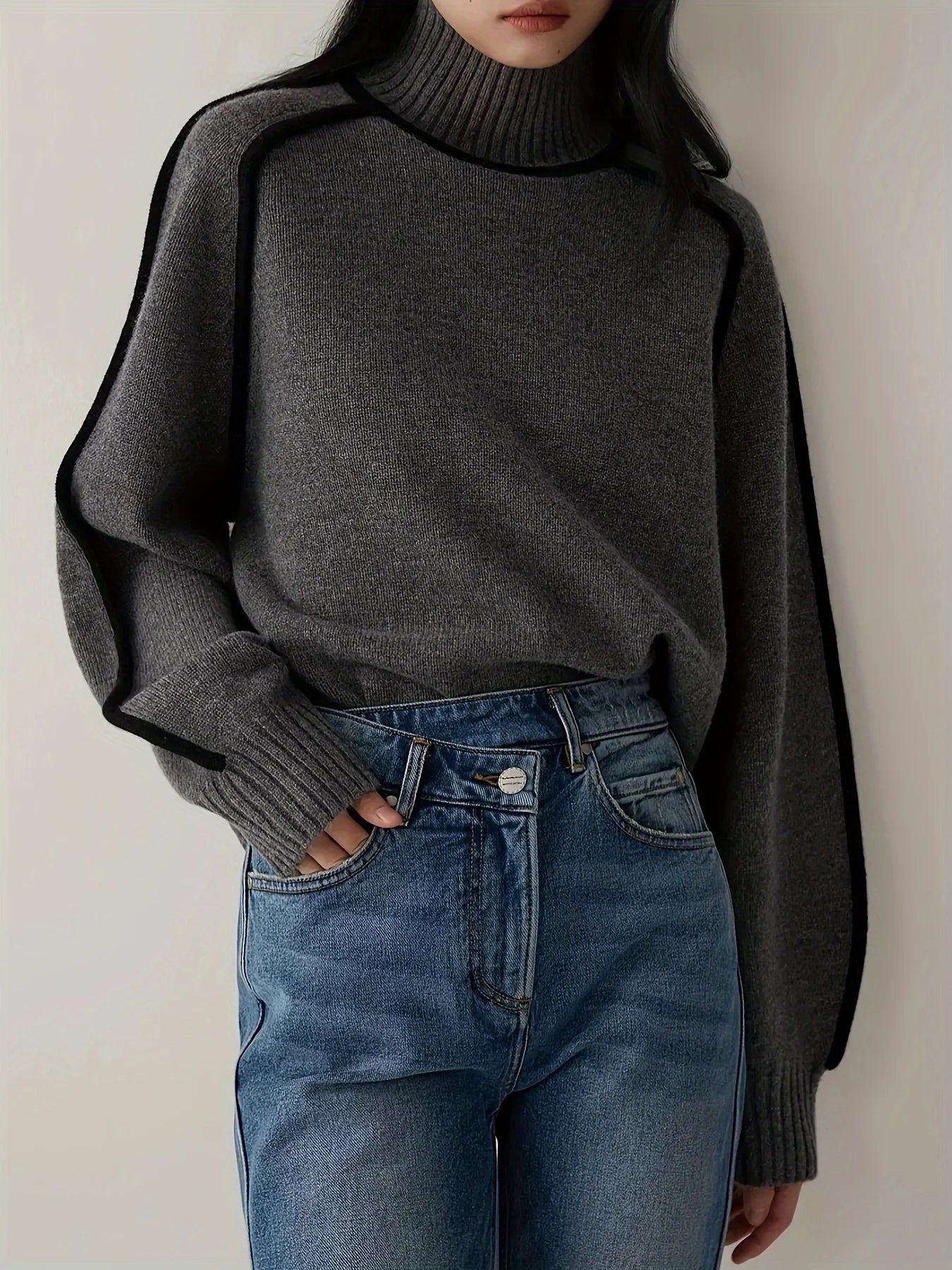Person wearing a dark gray sweater and blue jeans against a plain background